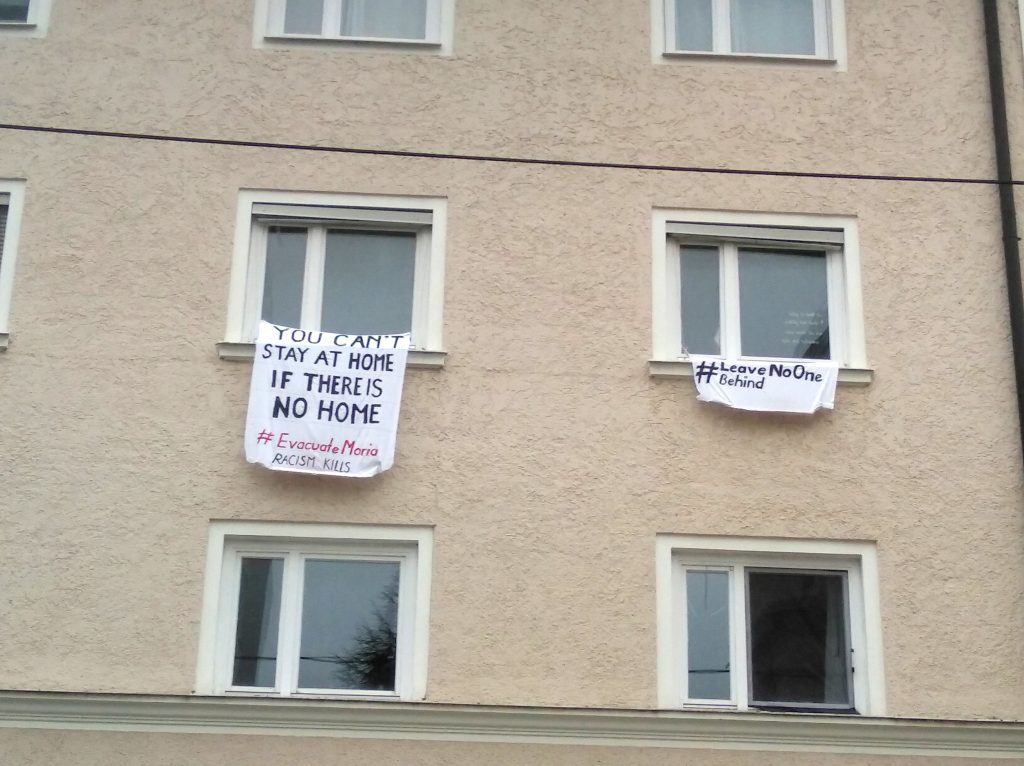 Zwei Transparente aus zwei Fenster. "You can't tsay at home if there is not home. #EvacucateMoria – Racism kills" und "#LeaveNoOneBehind"