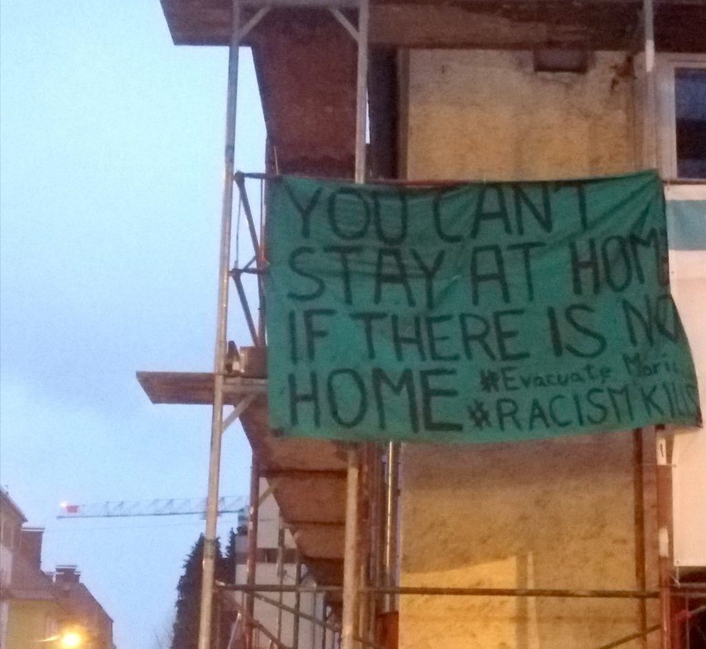 Transparent an einem Bau-Gerüst: "You can't stay at home if there is no home. #EvacucateMoria #RacismKills"