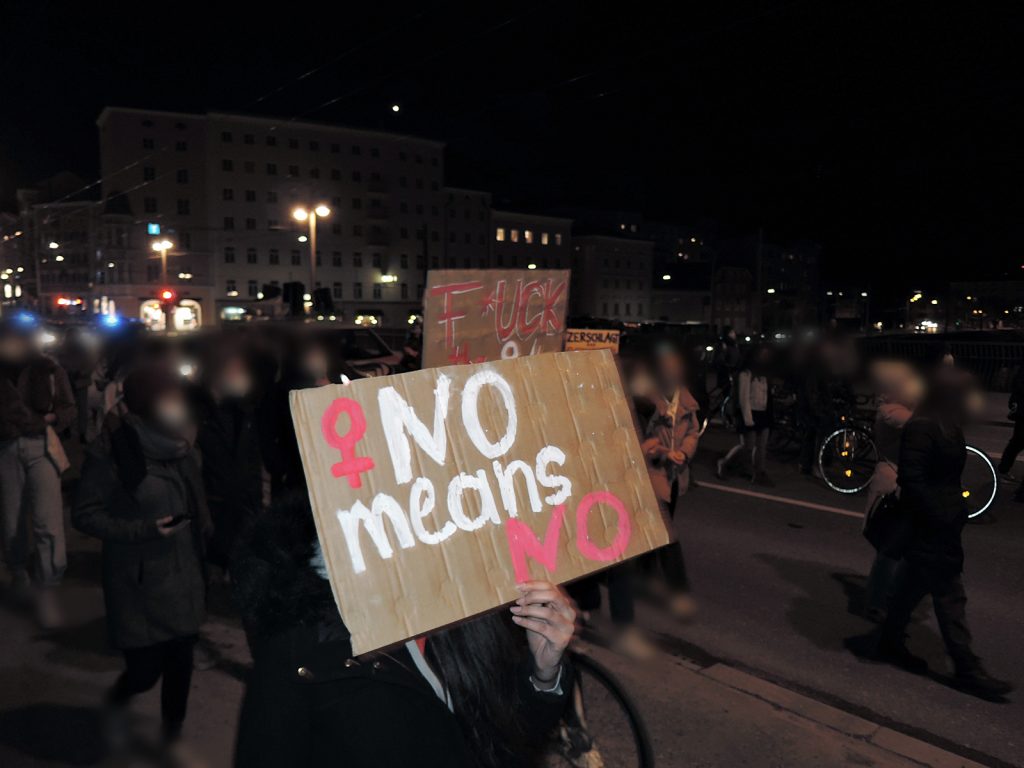 Aufnahme der Demo. Im Vordergrund hält eine Person ein Schild mit "No means no!" hoch. Im Hintergrund sieht man viele andere Demo-Teilnehmer_innen – alle sind unkenntlich gemacht.